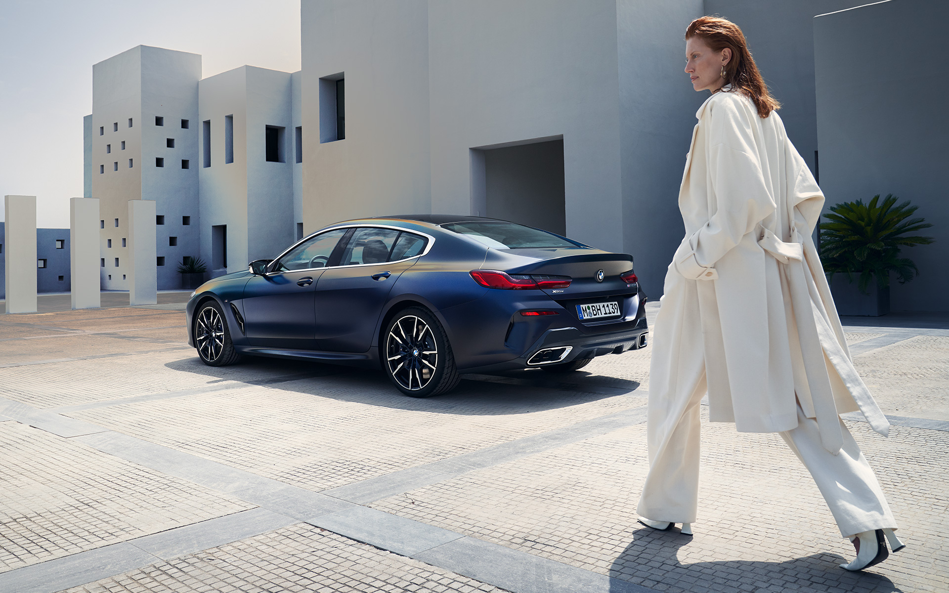 Jaunā BMW M850i xDrive Gran Coupé G16, LCI, atjaunināts, 2022, BMW Individual metāliska Frozen Tanzanite Blue krāsa, trīs ceturtdaļu aizmugures skats, ar modeli sievieti