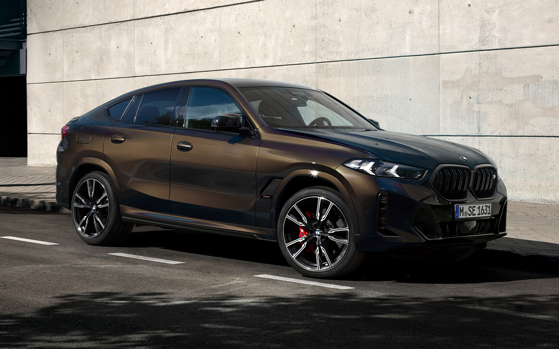 BMW X6 M60i, G06, BMW Individual metāliskā Pyrite Brown krāsā, divu trešdaļu sānskats, stāvvietā novietots automobilis